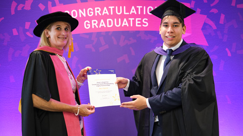 Two people in graduation attire; one hands a certificate to the other